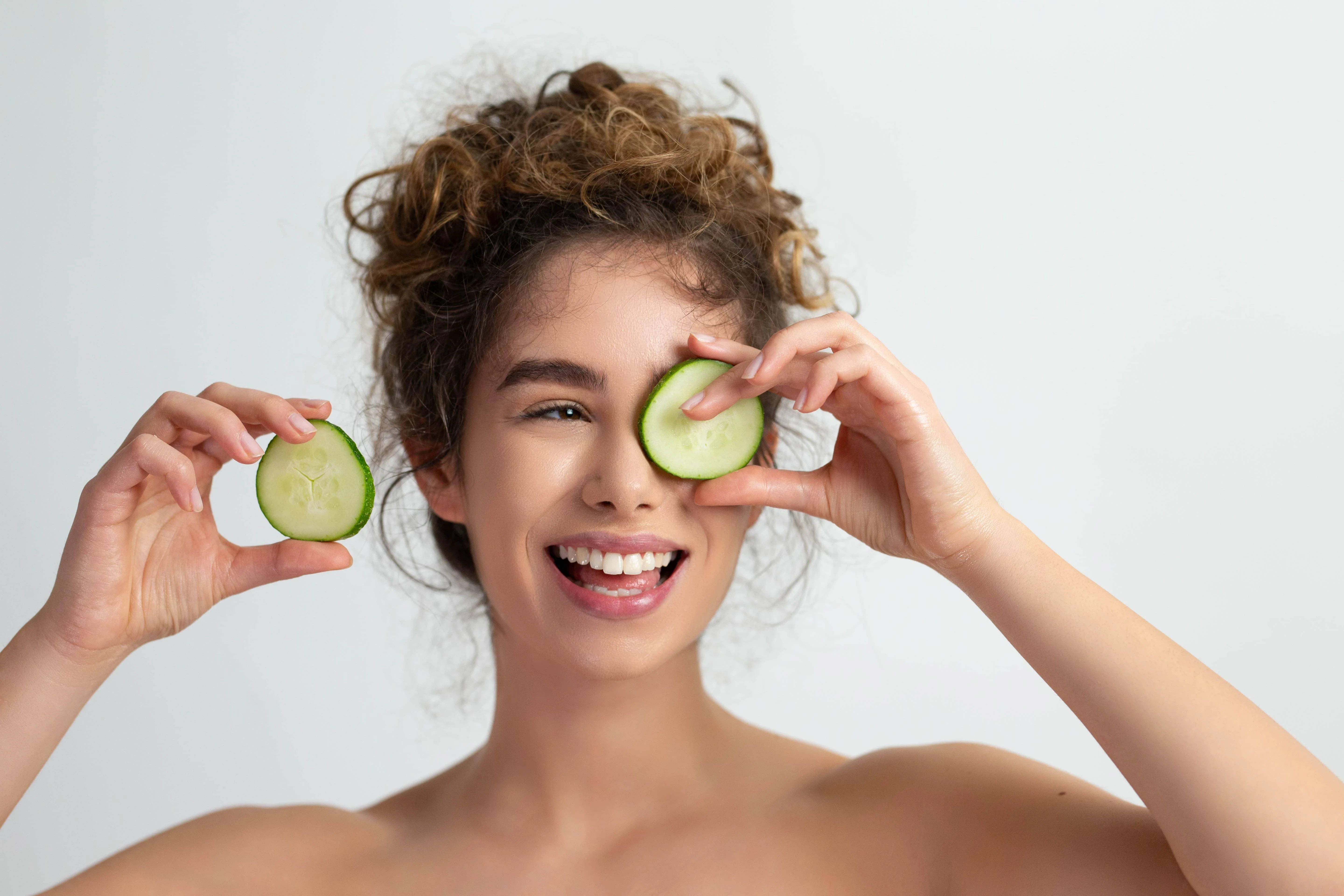  Lachende Frau mit Gurkenscheiben auf den Augen 