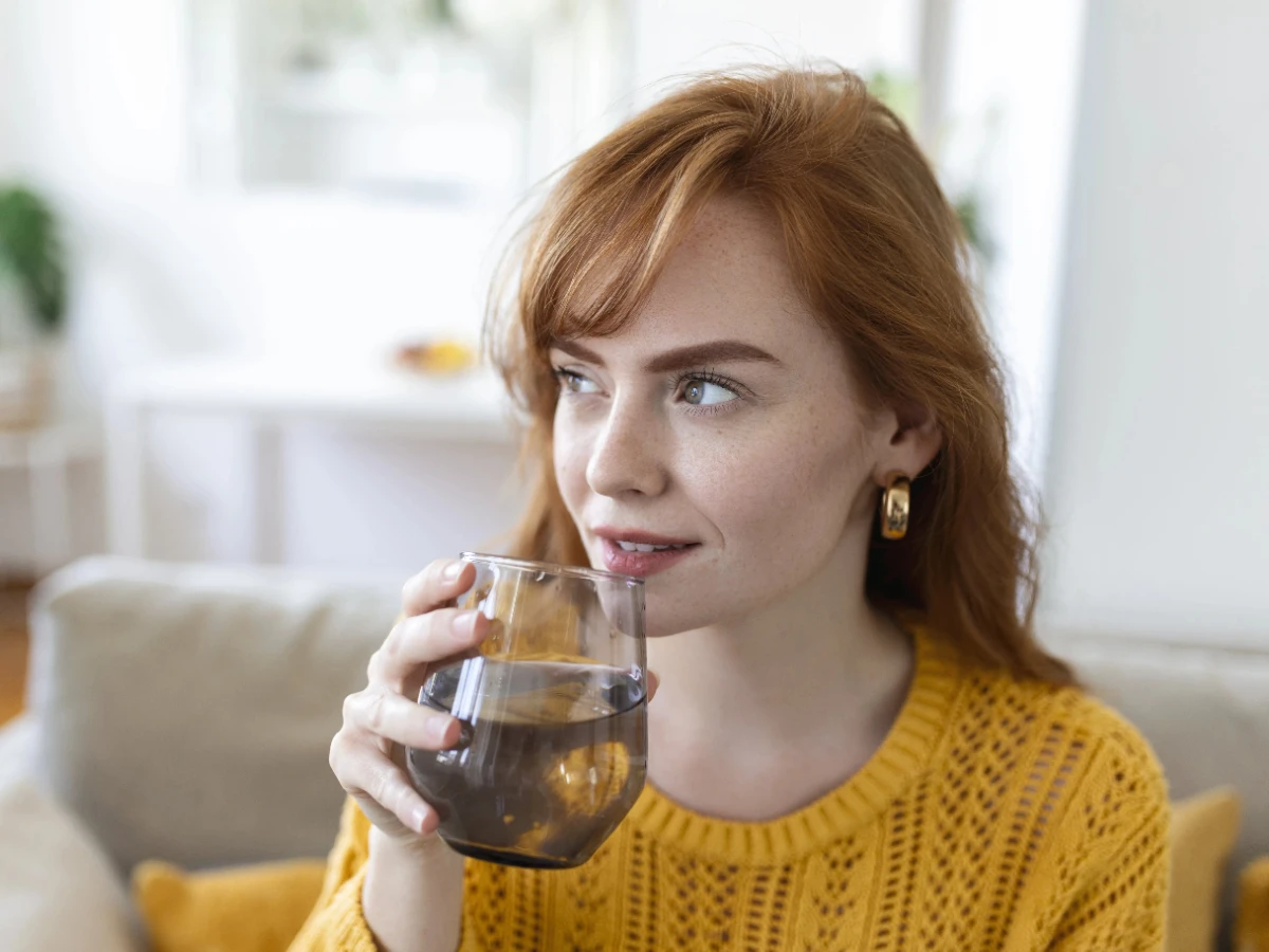  Frau trinkt Glas Wasser gegen trockene Haut 