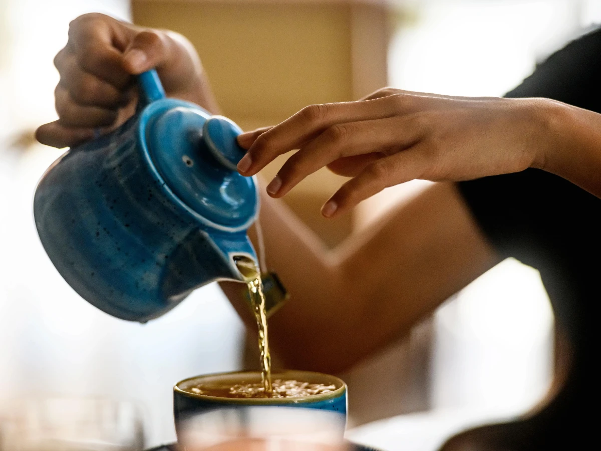  Tee wird aus einer Kanne in eine Tasse geleert 