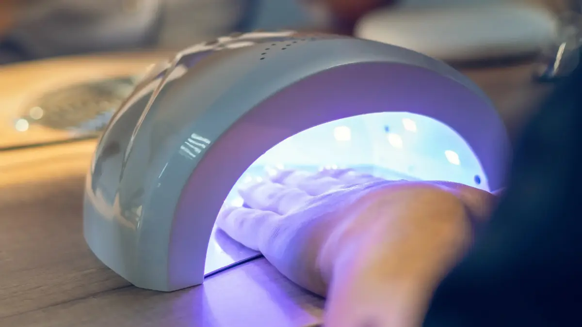  Frau hält ihre lackierten Gelnägel in die UV Lampe, damit das Gel aushärtet 