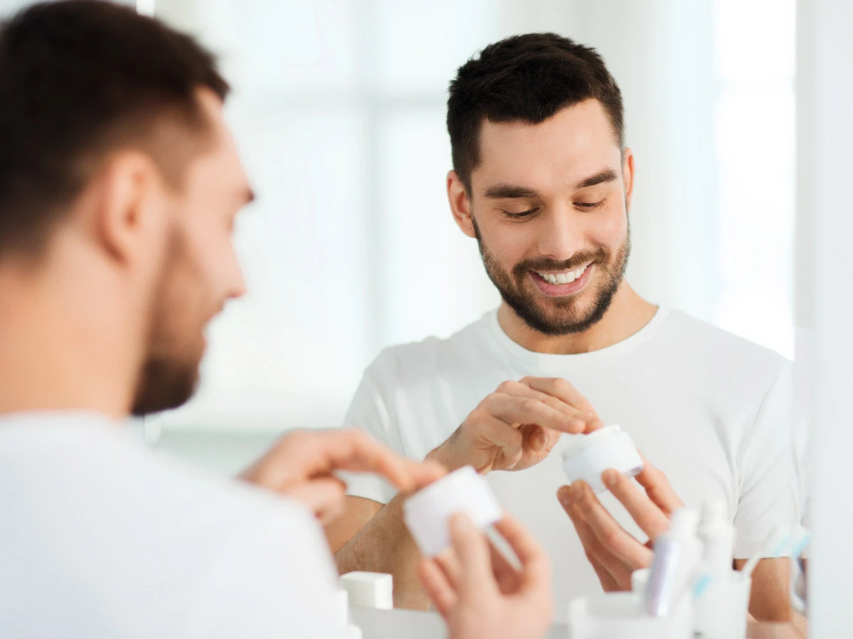  Junger Mann trägt Gesichtspflege auf im Badezimmer 