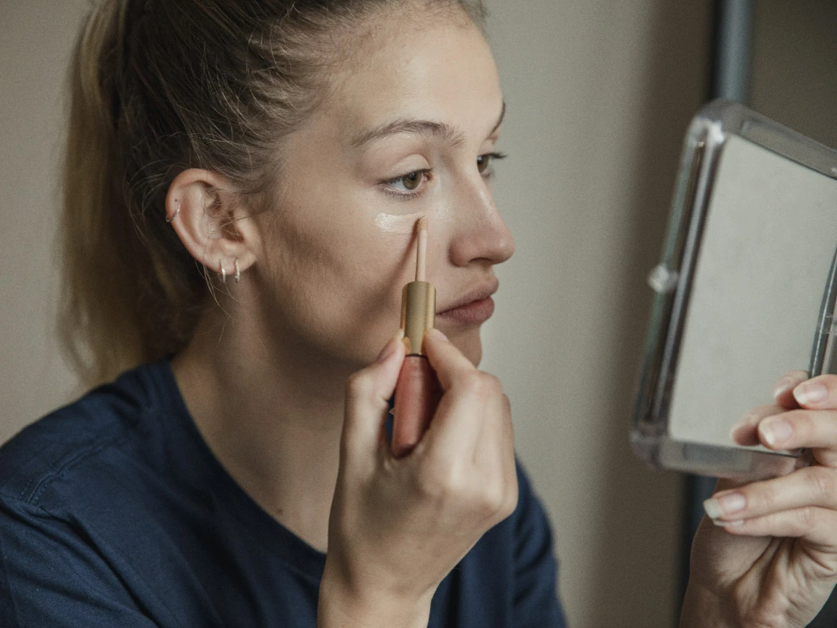  Frau schminkt sich und schaut in Handspiegel 
