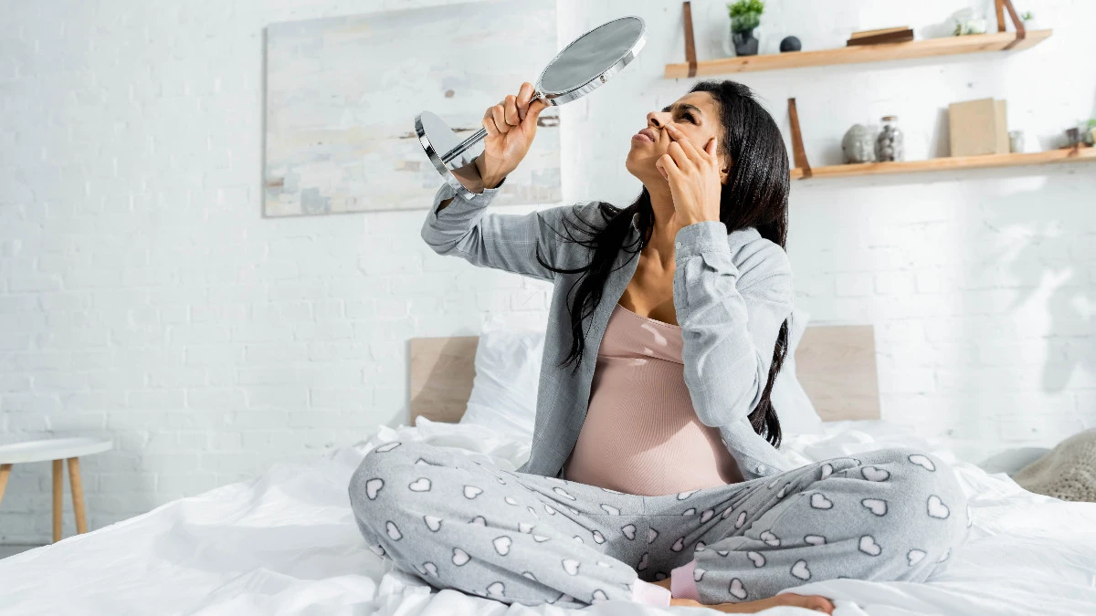  Schwangere Frau schaut skeptisch in Speigel wegen unreiner Haut 