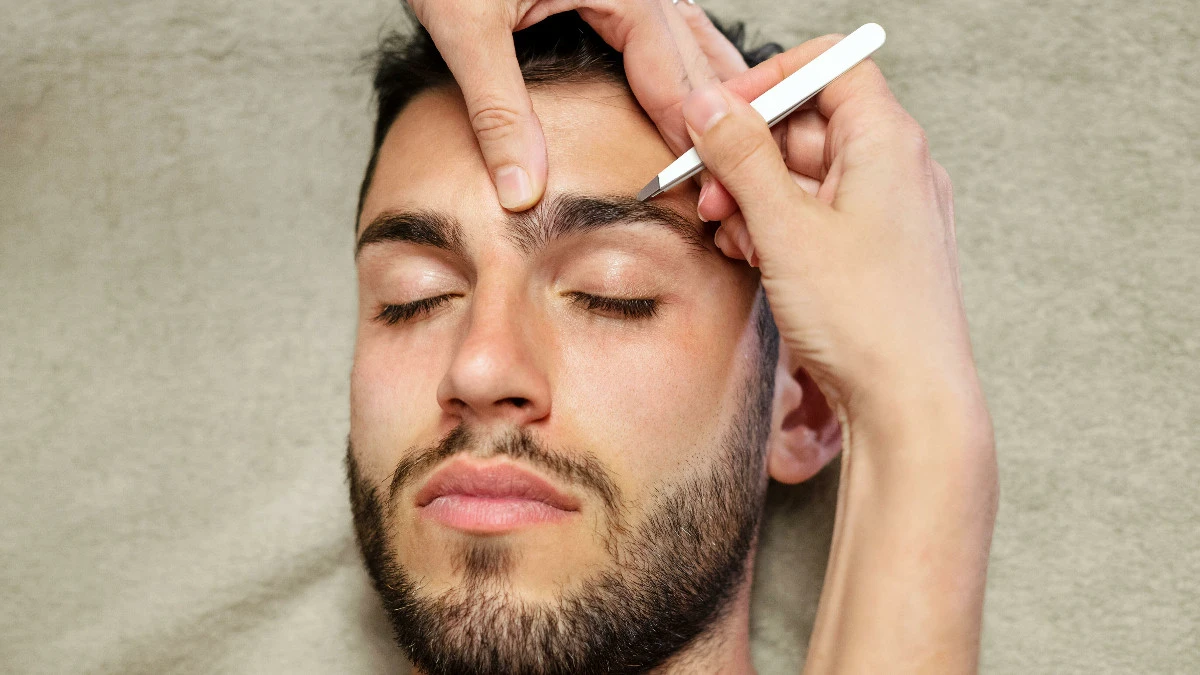  Einem Mann werden die Augenbrauen gezupft 